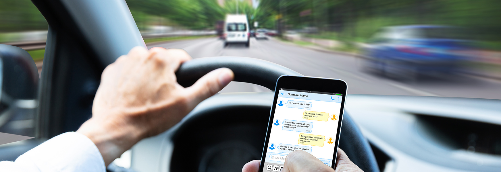 view of driver's hands texting while driving on busy city streets