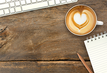Latte with heart-shaped foam on desk with keyboard and notebook