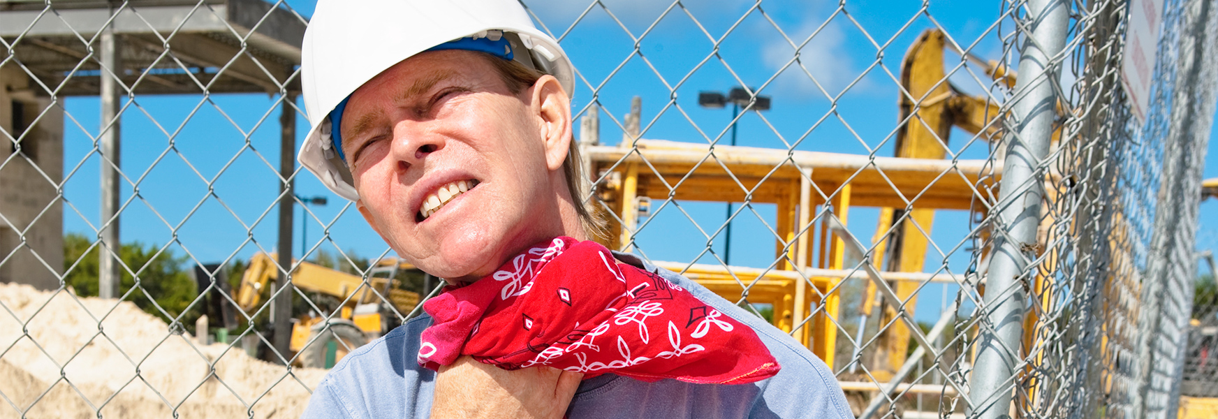 Man working in sun wiping sweat from neck with a bandanna 