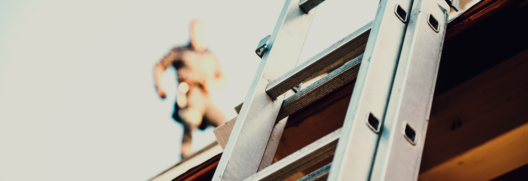 Ladder leaning on a building, out of focus worker walks on roof in background