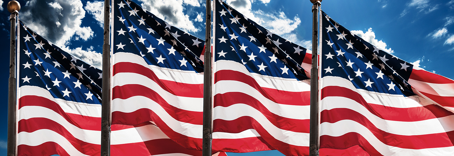 Four american flags blowing in the wind against a summer blue sky background