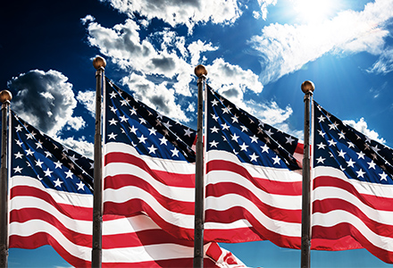 Four american flags blowing in the wind against a summer blue sky background