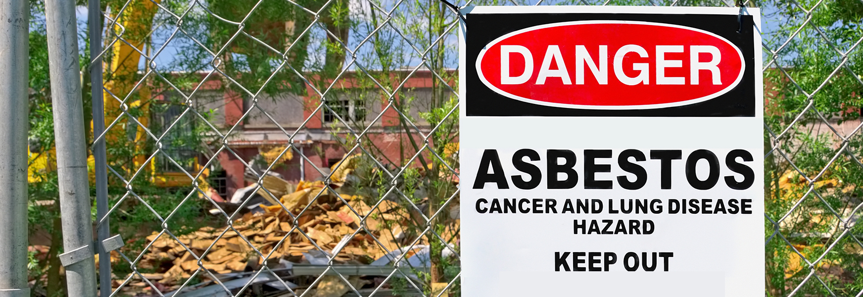 asbestos danger sign hung on fence in front of old building being demolished