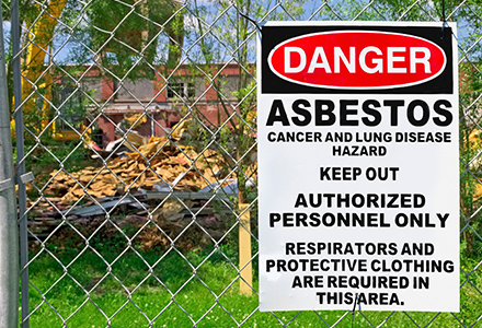 asbestos danger sign hung on fence in front of old building being demolished
