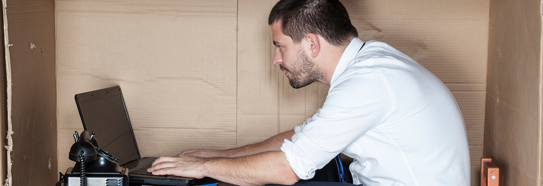 Man sits at a computer in a makeshift cubicle made out of cardboard