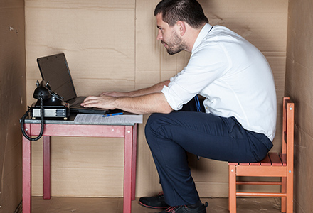 Man sits at a computer in a makeshift cubicle made out of cardboard