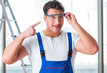 Young male worker pointing at safety glasses worn on his face.