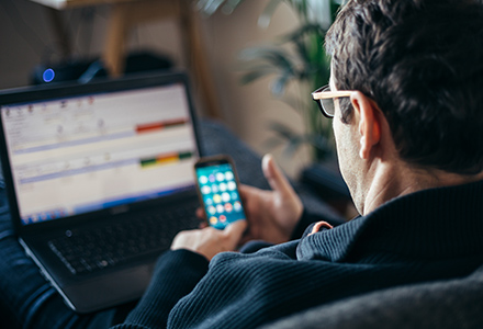 Man checks his cellphone while working at home with laptop on his lap