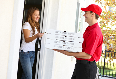 Woman greeting pizza delivery driver at front door.