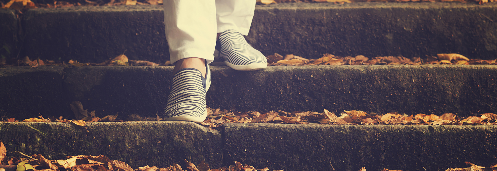 Legs walking down leaf-covered stone steps