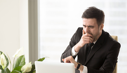 Office worker using computer and yawning at desk.