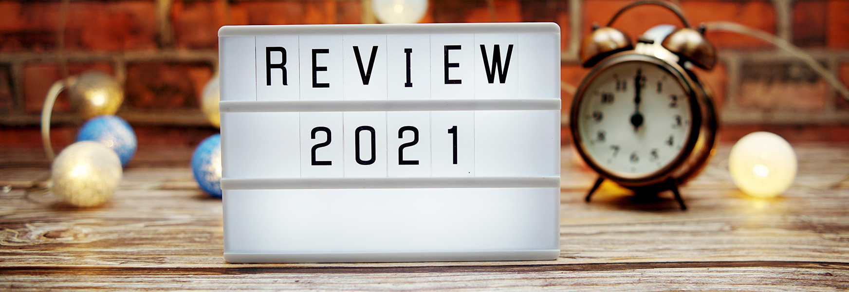 Marquee sign reading "Review 2021" on wooden tabletop against festive brick background