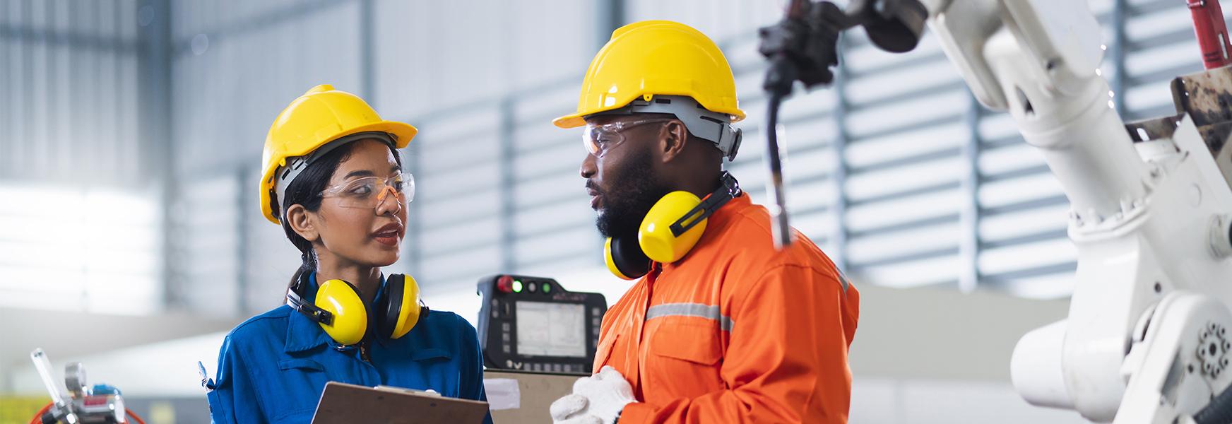 Workers wearing safety equipment having a conversation on factory production floor