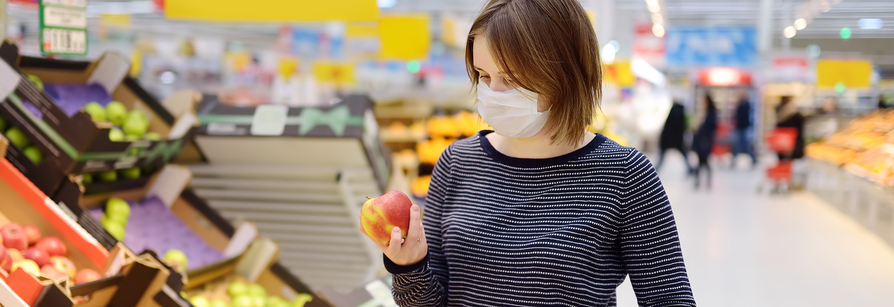Young woman wearing a mask, shopping for fruit at a supermarket
