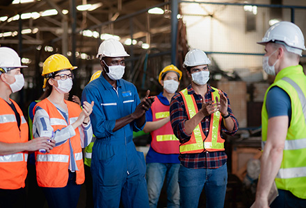 Masked factory workers having a standup meeting
