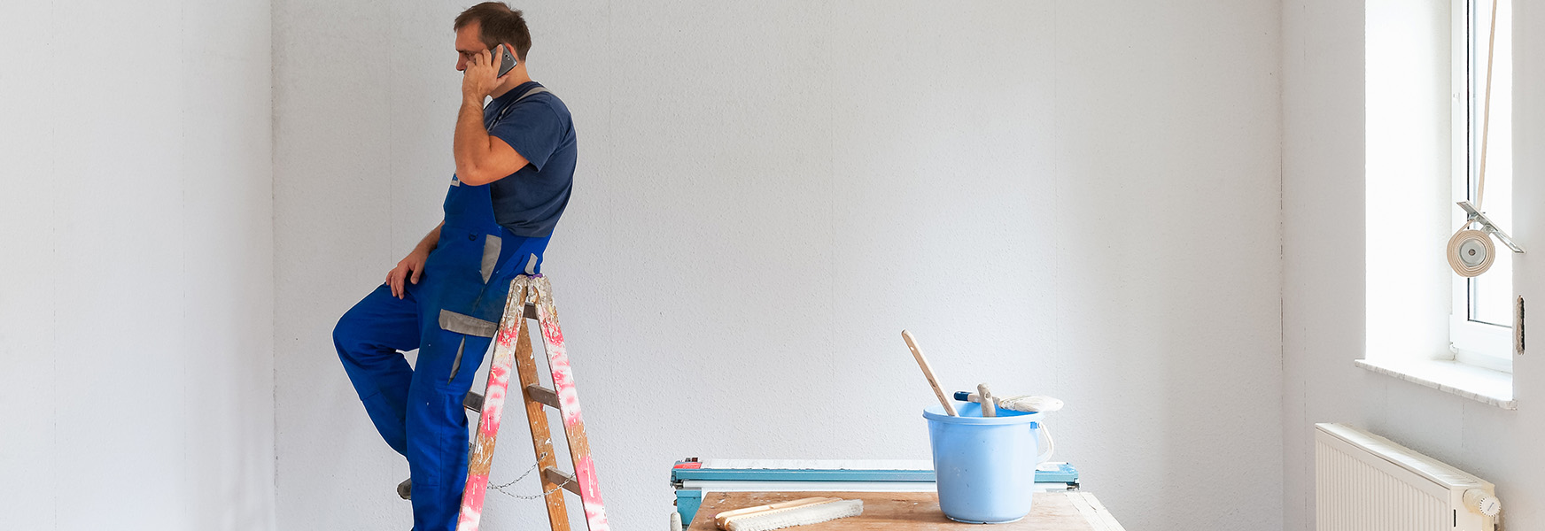 Painter sitting on ladder, talking on cellphone.