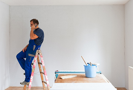 Painter sitting on ladder, talking on cellphone.