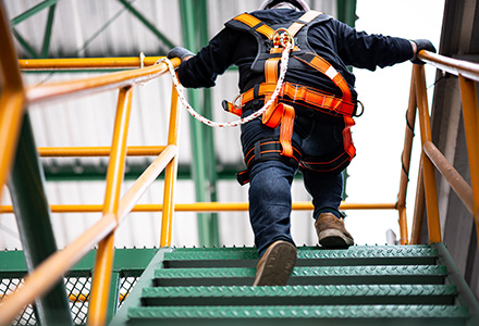 Worker climbing stairs with fall arrest harness attached