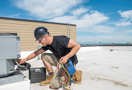 Worker inspecting HVAC unity on rooftop