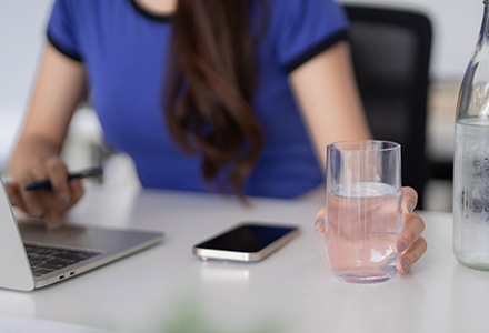 Woman in office reaching for a glass of water