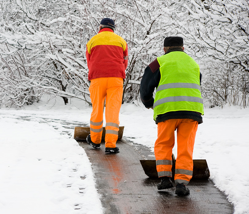 Workers in high visibility gear shoveling snowy walkway