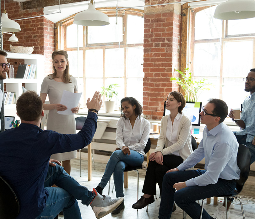 Man raising hand to ask question to diverse workers in office