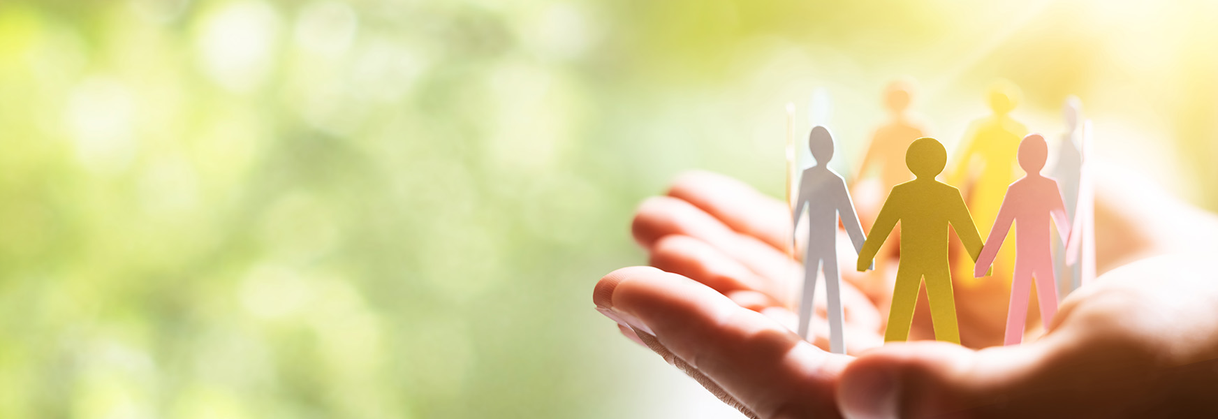 Cupped hands holding paper people joining hands in a circle