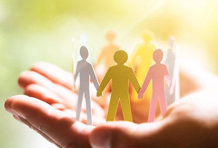 Cupped hands holding paper people joining hands in a circle