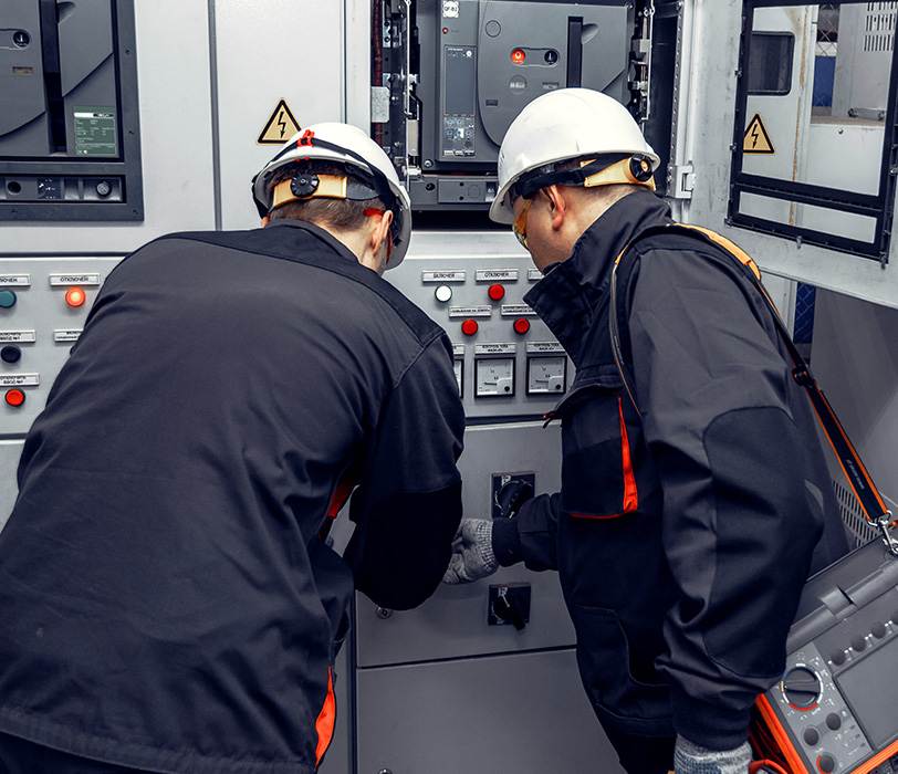 Two technicians wearing PPE inspecting electrical control panel