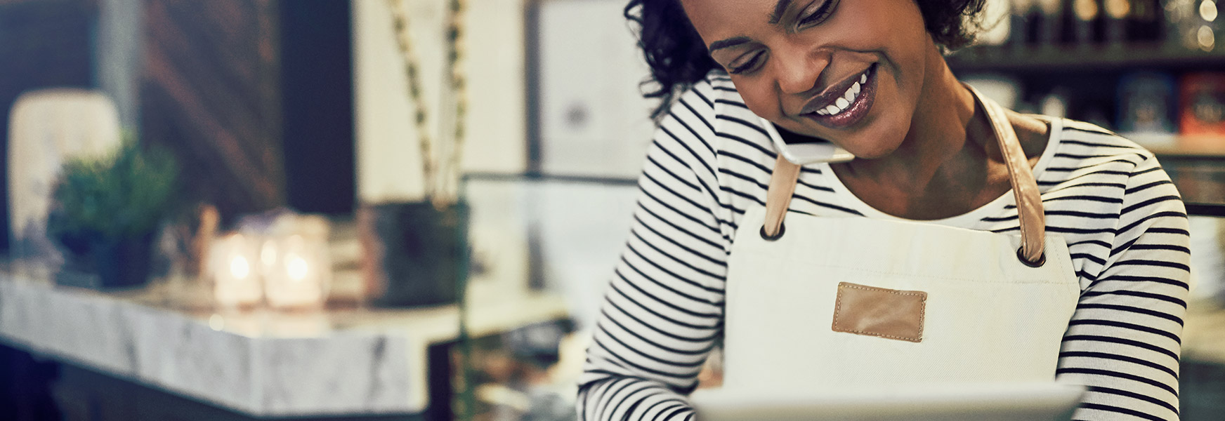 Happy small business owner talking on phone while using tablet