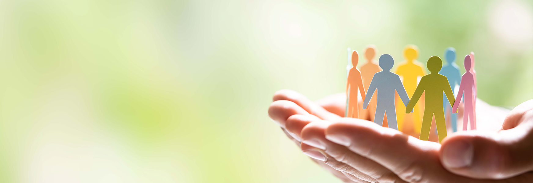 Open hands holding paper human figures locking hands in a circle against out of focus green background