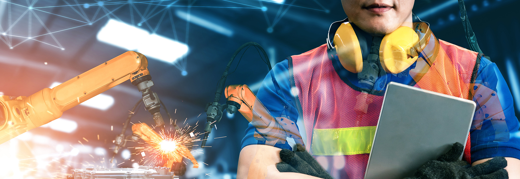 Woman wearing personal protective equipment and holding clipboard standing with arms crossed standing in factory with machinery sparking behind her.