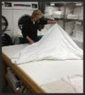 Laundry worker folding large piece.